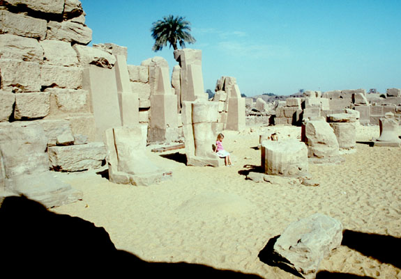 Pylon V from the West. The girl is sitting on the feet of a broken Osiride statue